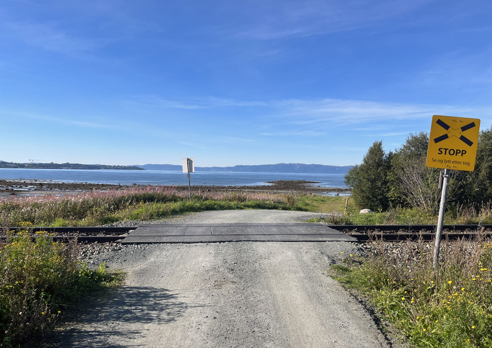 Enkel planovergang i kystlandskap med havet i bakgrunn.