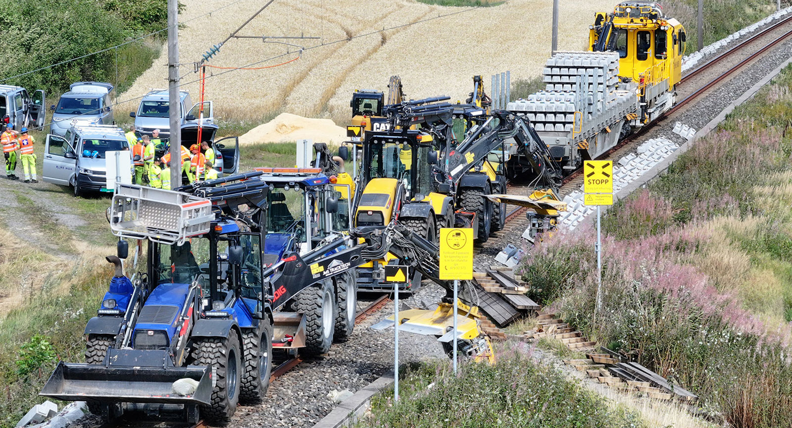 Skinnetraktorer og maskiner står parkert i sporet, mens en gruppe arbeidere står ved siden av.