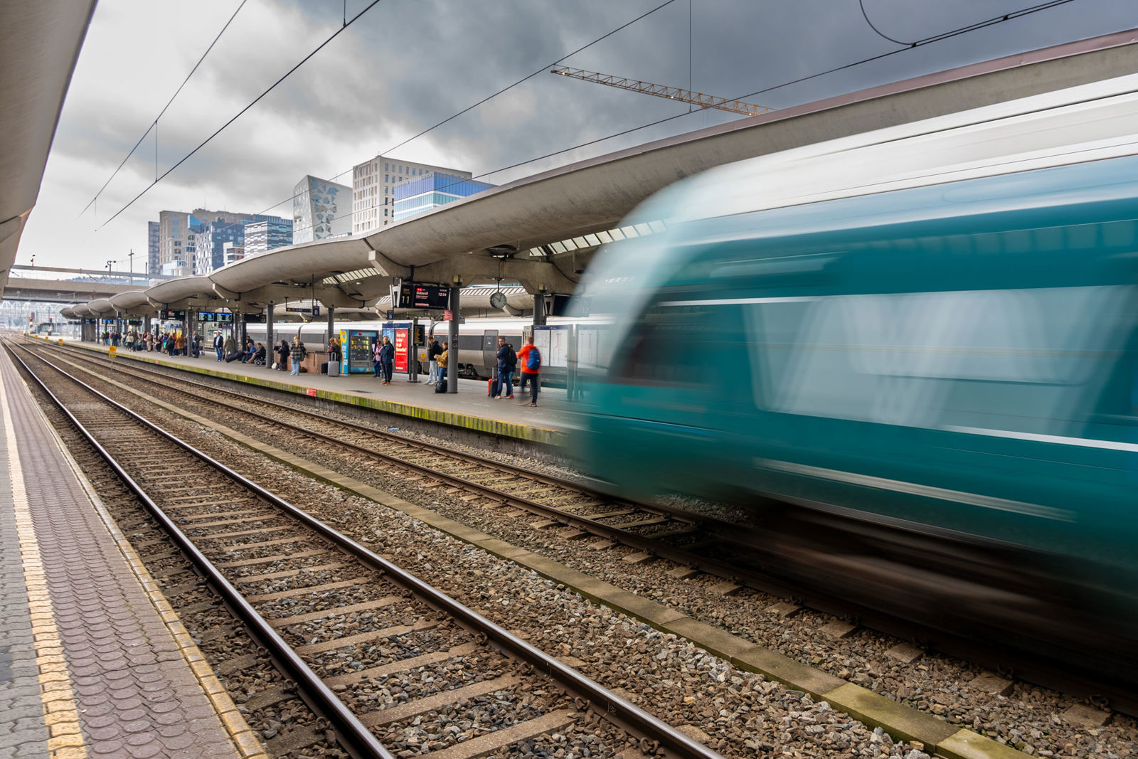 Et grønt Vy-tog kjører inn til plattform på Oslo S. Passasjerer og andre tog i bakgrunnen.